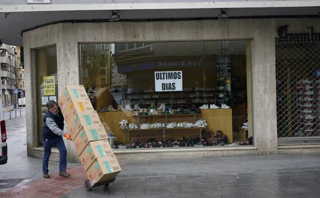 Un empleado transporta unas cajas frente a una tienda cerrada.