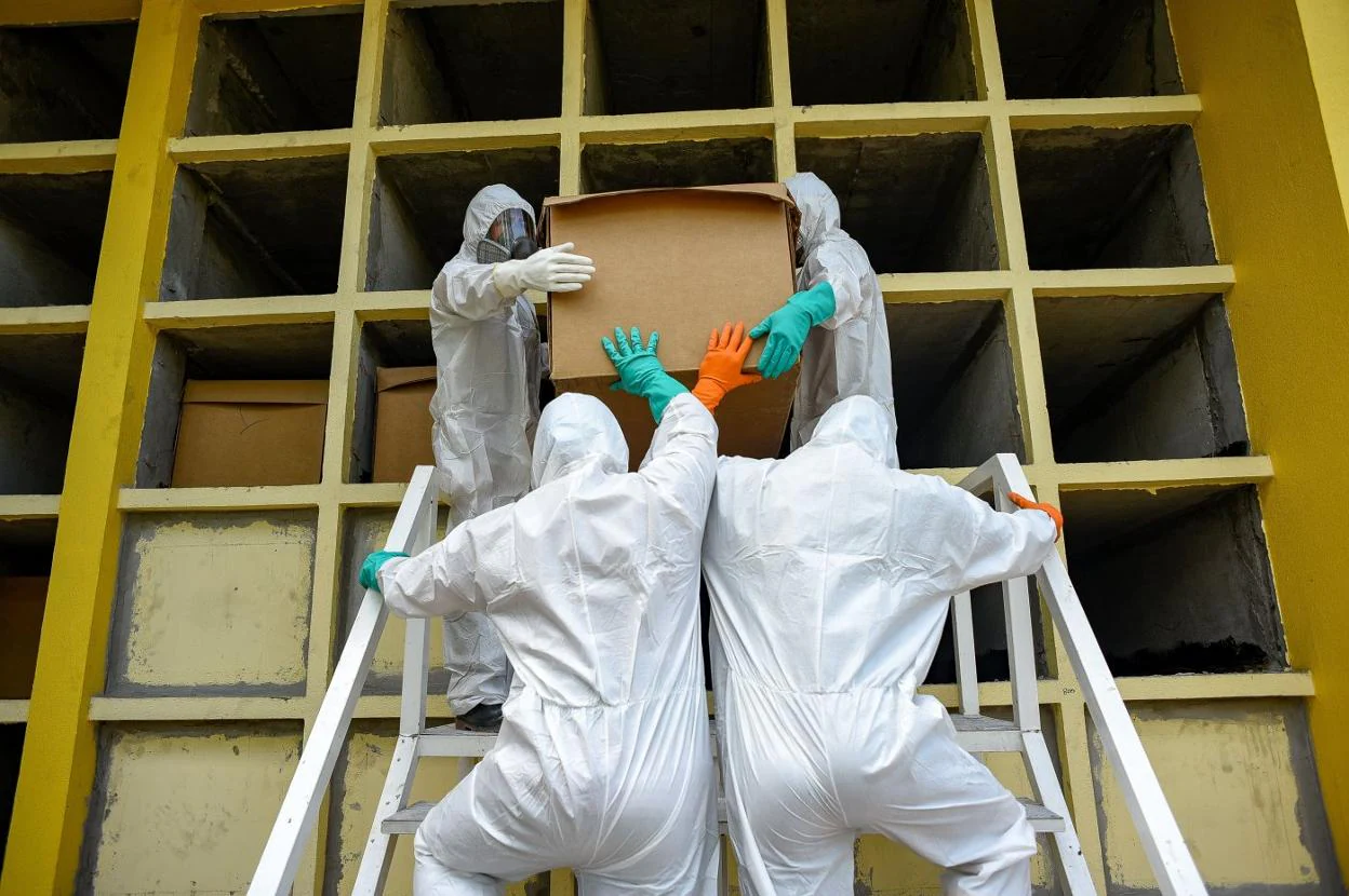 Trabajadores del cementerio Parques de la Paz, del Estado ecuatoriano de Guayas, meten una caja de cartón con un fallecido en un nicho. mauricio torres/ EFE