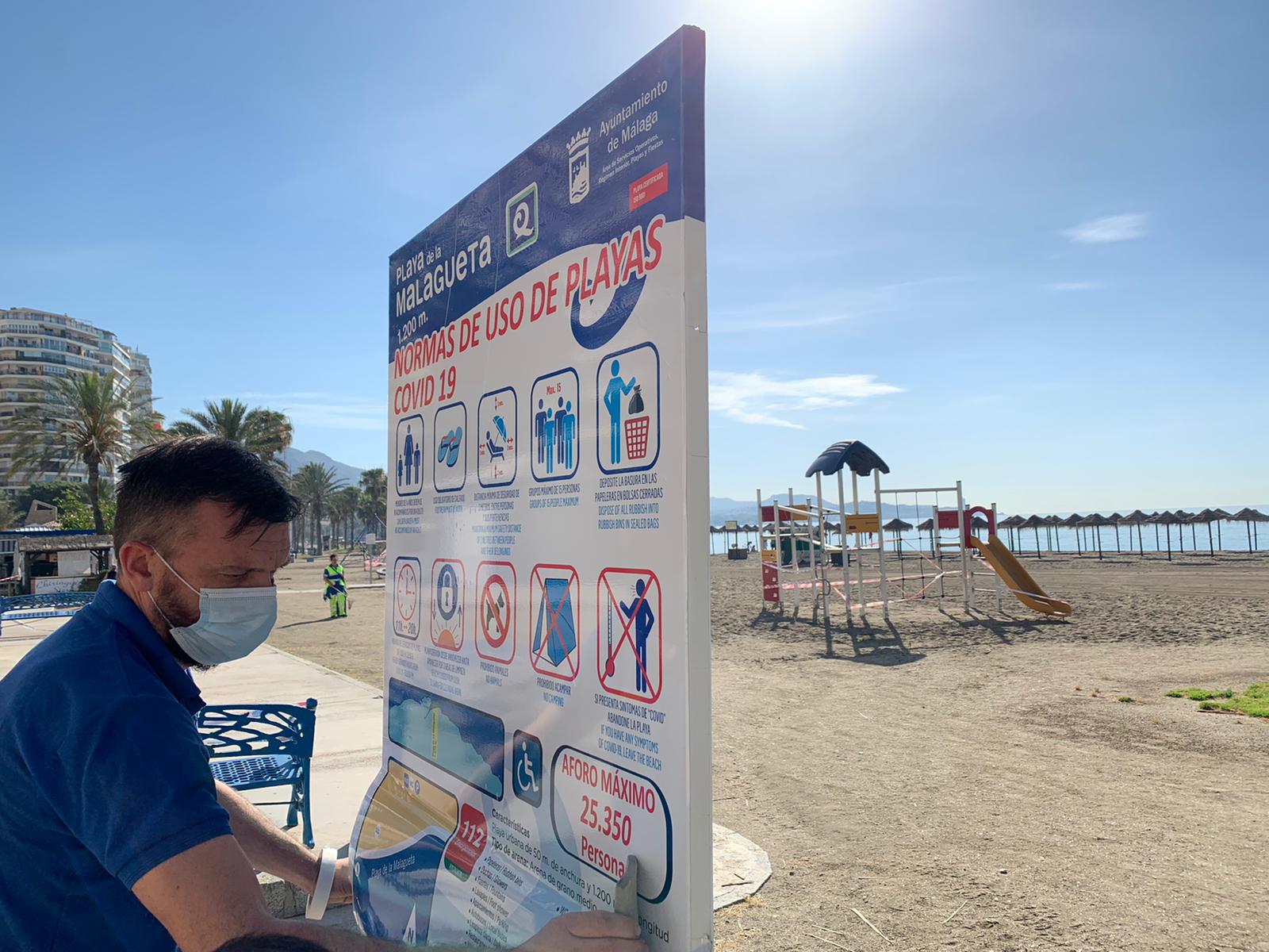 Operarios colocan carteles informativos sobre el uso de las playas en La Malagueta.