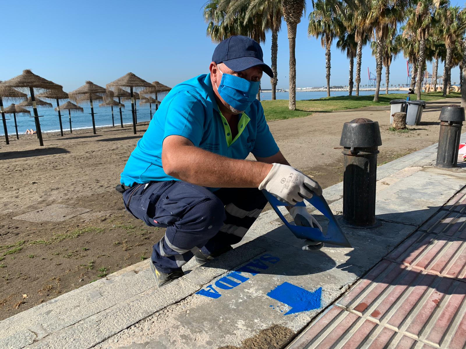 Operarios colocan señales en el suelo para indicar los accesos de entrada y salida a la playa en La Malagueta.