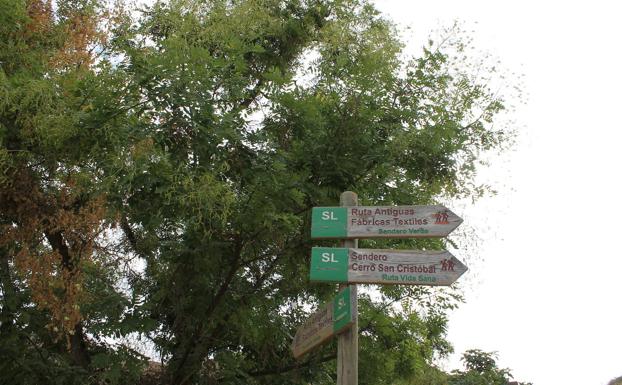 Imagen principal - Arriba, señales indicativas de esta ruta. Abajo, a la izquierda, los primeros metros discurren por la acera, y, a la derecha, señales en el punto donde el carril de tierra llega a la carretera.