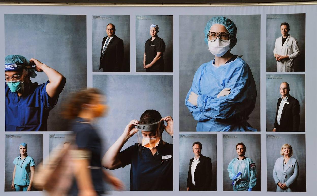 Una mujer pasa junto a una exposición de fotografías al aire libre sobre trabajadores sanitarios 