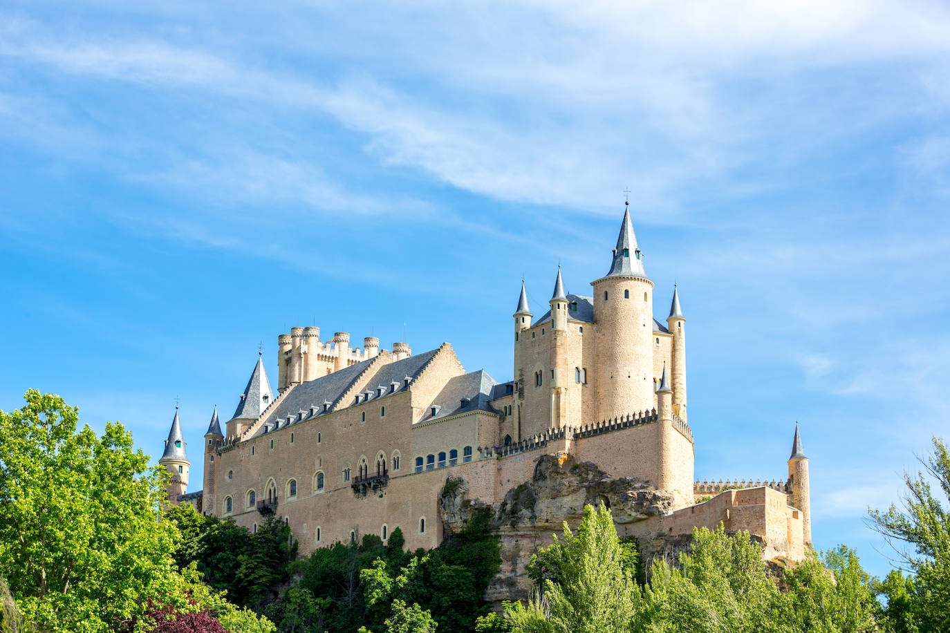 Alcázar de Segovia (España). Este sitio declarado Patrimonio de la Humanidad por la UNESCO es uno de los castillos-palacios más distintivos de toda España y de Europa. En lo alto de la ciudad, sus muros son testigos privilegiados de la historia de España. Austero, como lo eran los reyes castellanos, elevado sobre la roca en la confluencia de los valles del Eresma y el Clamores, parece guardar la ciudad. Su bella Torre del Homenaje, a menudo comparada con la proa de un barco navegando entre los ríos, es de una belleza impresionante. Los turistas comprueban admirados que la fortaleza forma una parte viva de esta ciudad castellana, elegida como lugar de residencia por muchos de los monarcas de la dinastía Trastámara. Vale la pena visitar el Salón de Ajimeces con su colección de obras de arte, el Salón de los Reyes y el Salón del Trono. Pero hay que dedicar tiempo a curiosear el exterior y contemplar su espectacular perfil desde el borde del Eresma, según detallan desde la web Jetcost.es