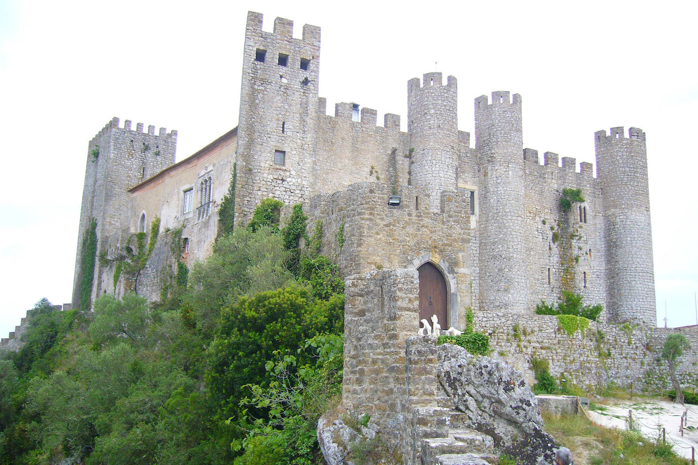 Castillo de Óbidos (Portugal). La construcción de este castillo mágico se remonta a la presencia romana en Portugal. El castillo de Óbidos tiene torres en forma de cilindro y cuadradas, mientras que la piedra caliza y el mármol añaden una faceta grandiosa a la fachada. Es un buen ejemplo de una fortificación bien conservada, y el castillo ha escapado al destino de ser convertido en ruinas, y se ha transformado, según Jetcost.es en uno de los hoteles pequeños más románticos de Portugal. El pueblo que lo rodea, Óbidos, es conocido por sus atractivos paisajes y exuberante vegetación. El que una vez ofreció protección militar en el corazón de Portugal, ahora ofrece como hotel a los visitantes la oportunidad de viajar en el tiempo, según la web Jetcost.es