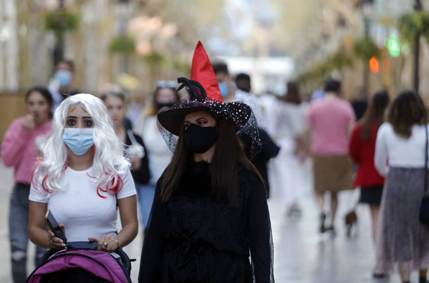 Personas disfrazadas se mezclan con las que llevan mascarillas en un paso de peatones en Málaga capital.