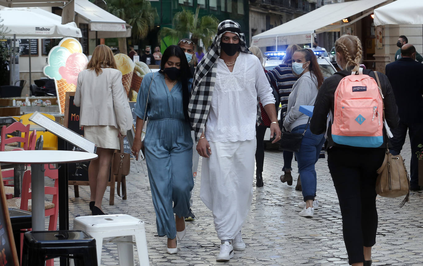 Personas disfrazadas se mezclan con las que llevan mascarillas en un paso de peatones en Málaga capital.