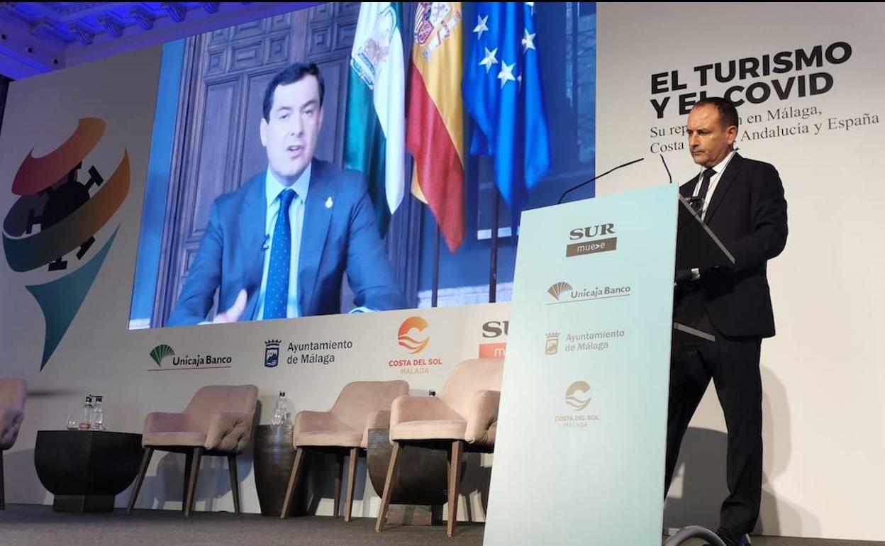 El director de SUR, Manolo Castillo, atiende desde el atril al presidente de la Junta durante su intervención telemática en el foro.