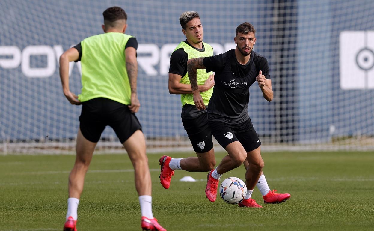 El jugador del Málaga, Cristian, conduce un balón durante un entrenamiento con Mejías al fondo.