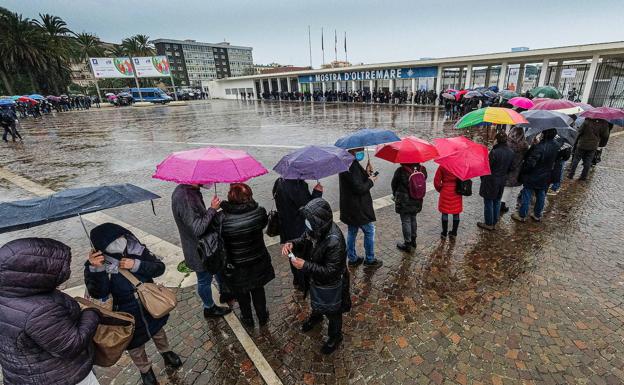 una larga cola de personas esperan bajo la lluvia para vacunarse en Nápoles.