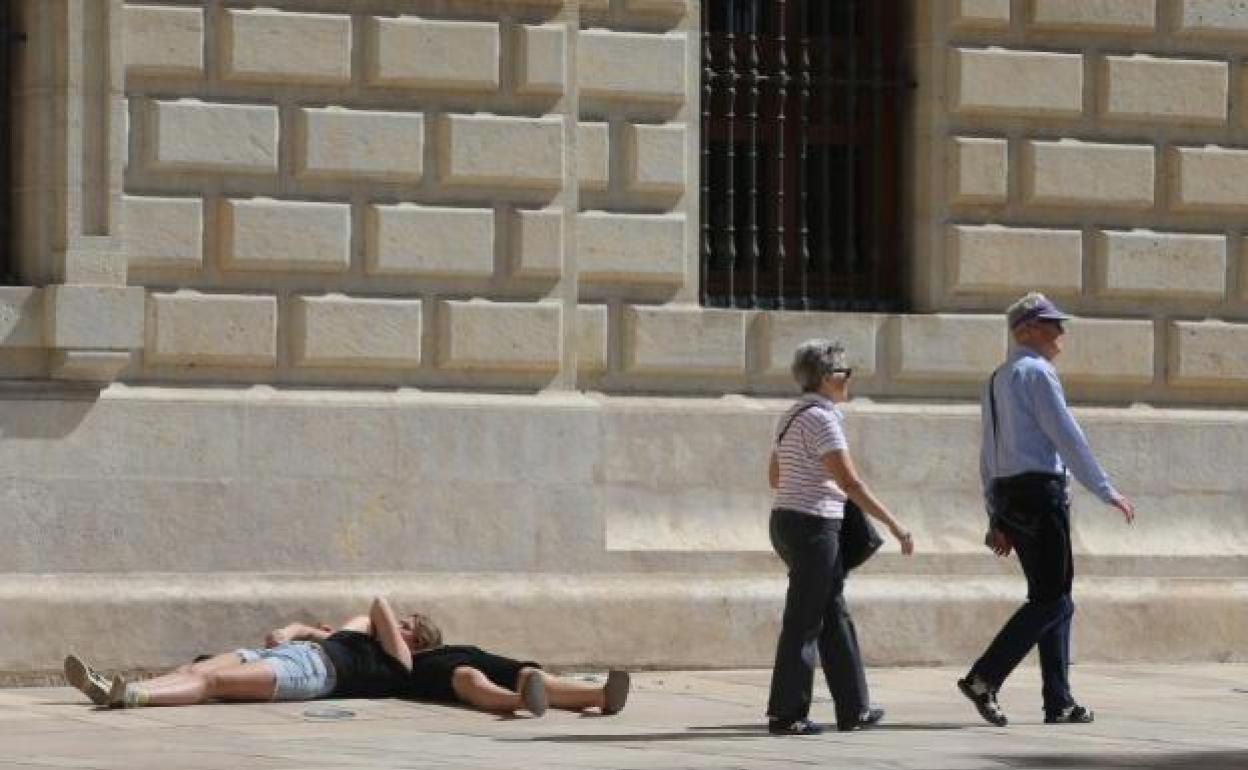 Turistas tumbados al sol en plena calle Alcazabilla, junto al Museo de la Aduana de la capital