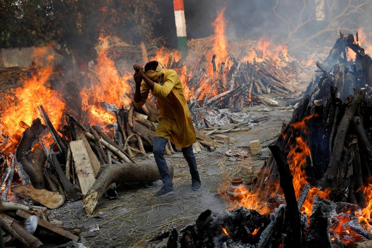 Un hombre pasa corriendo junto a las piras funerarias de víctimas de coronavirus durante una cremación masiva en Nueva Delhi. reuters