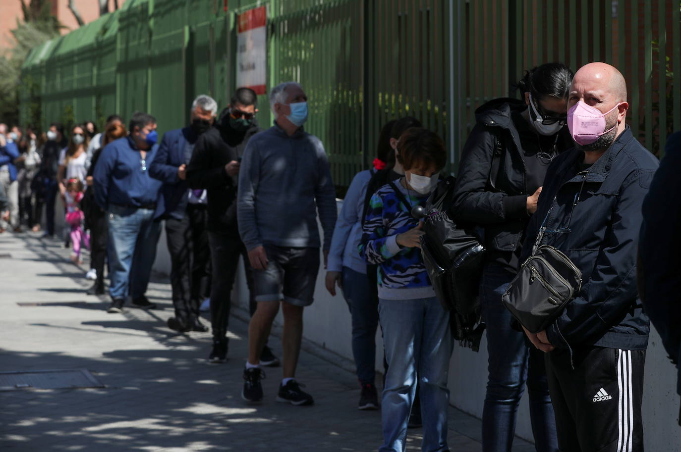 Los votantes, con máscaras protectoras y manteniendo la distancia social, hacen cola para acceder a un colegio electoral.