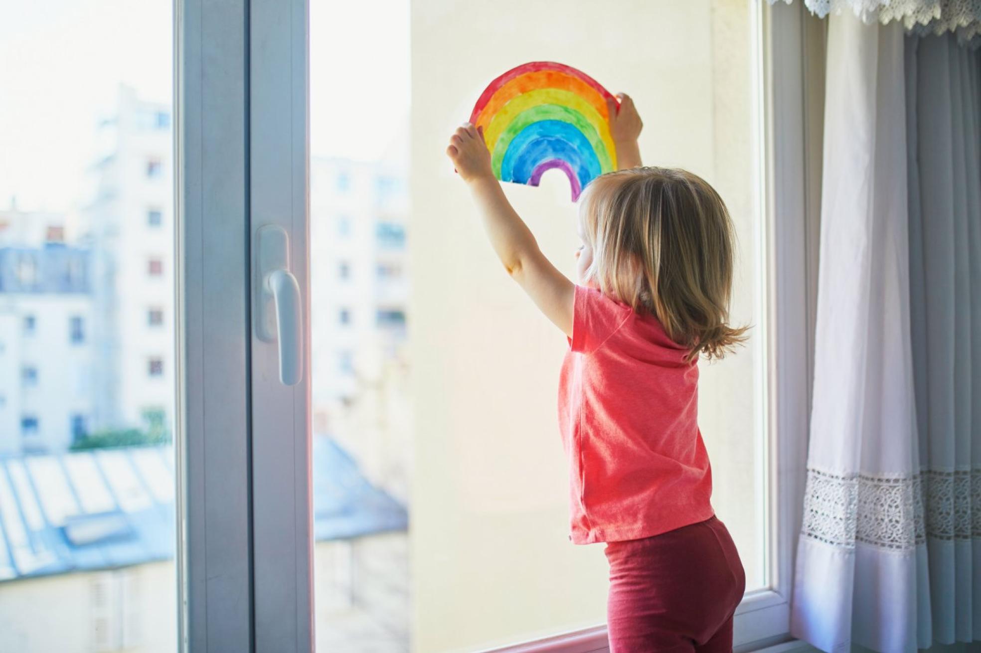  Una niña coloca el dibujo de un arco iris contra el cristal de una  ventana.   e. POKROVSKY 