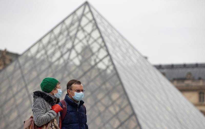 Dos personas caminan junto a la pirámide del Louvre. 