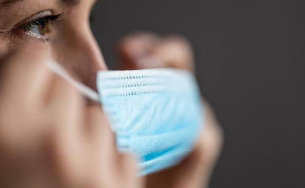 Una mujer se pone una mascarilla higiénica. 