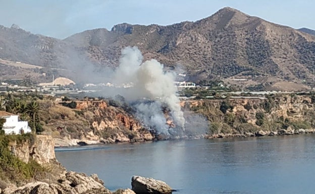 Imagen principal - Arriba, imagen de las llamas en los acantilados de Nerja vistas desde el Balcón de Europa; abajo a la izquierda, el helicóptero del Infoca descargando agua junto a unas casas, y a la derecha, los bomberos del Consorcio Provincial, junto a una de las viviendas.