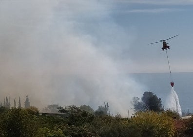 Imagen secundaria 1 - Arriba, imagen de las llamas en los acantilados de Nerja vistas desde el Balcón de Europa; abajo a la izquierda, el helicóptero del Infoca descargando agua junto a unas casas, y a la derecha, los bomberos del Consorcio Provincial, junto a una de las viviendas.