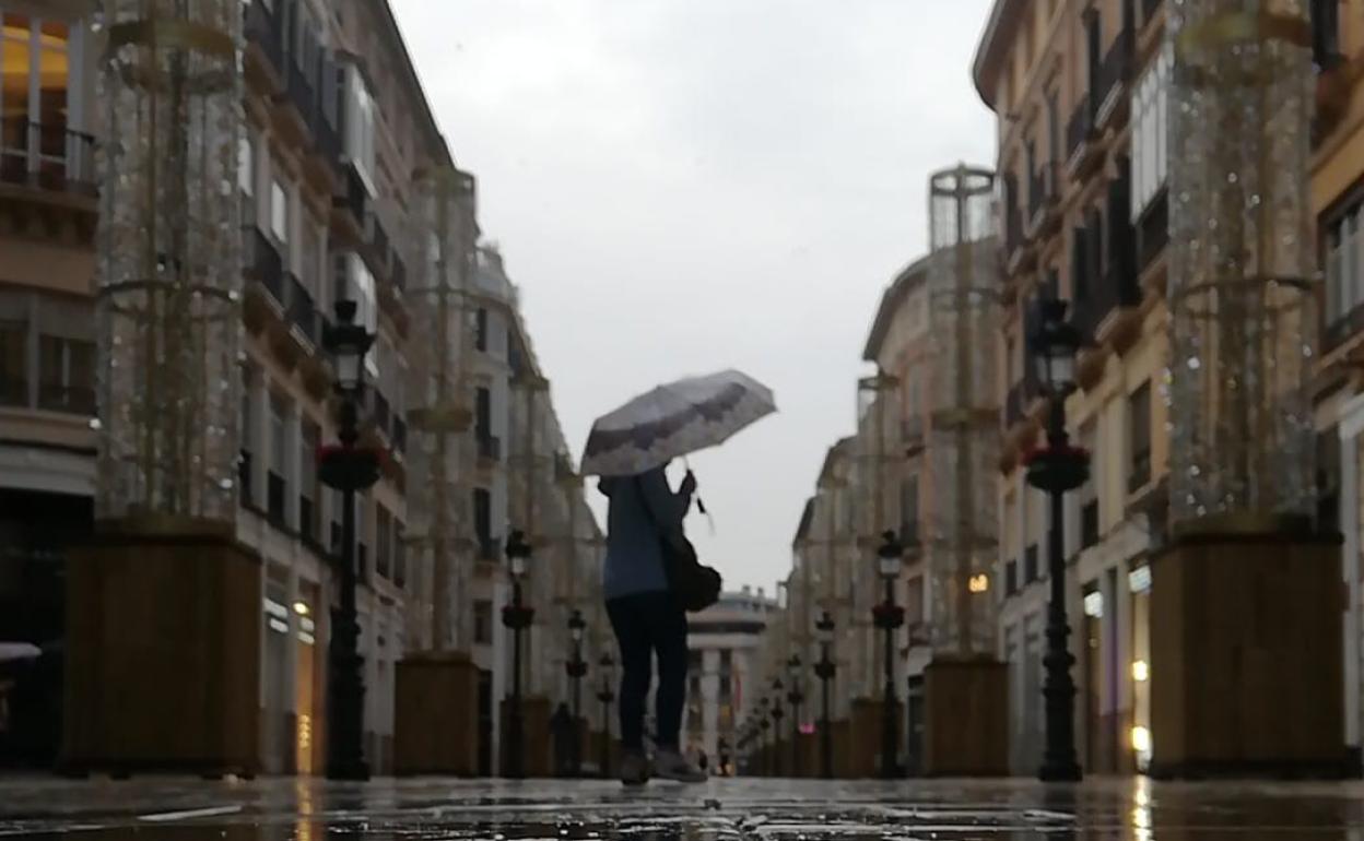 Una persona camina bajo la lluvia en la calle Larios de Málaga. 