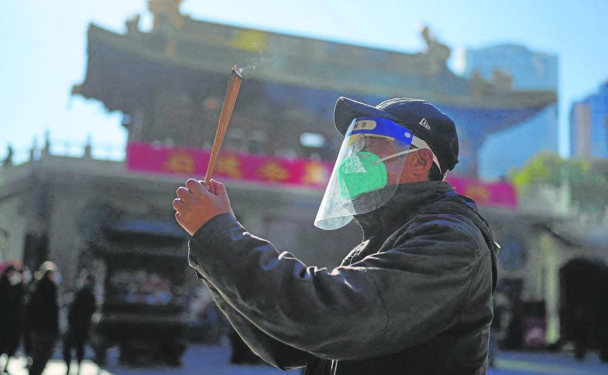 Un hombre con máscara protectora y careta rinde culto en el templo budista de Jingan.