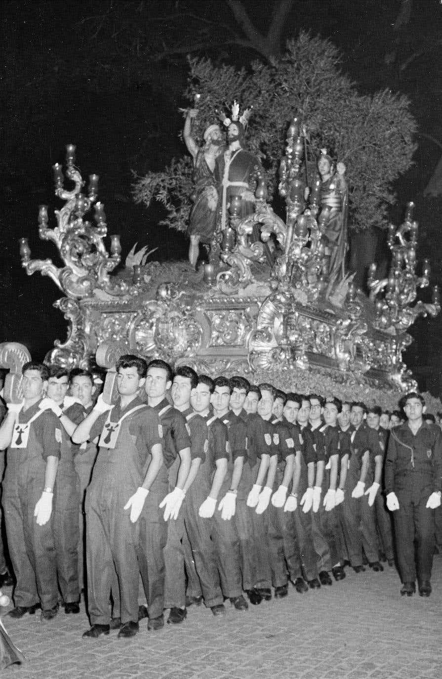 La Cofradía del Prendimiento estuvo íntimamente ligada a la antigua Escuela de Formación Profesional Francisco Franco. En la imagen se observan a sus alumnos, ataviados con el característico mono de trabajo, portando el trono de Jesús del Prendimiento. Tanto las imágenes como las andas son obras del tallista e imaginero malagueño Pedro Pérez Hidalgo, que las realizó entre 1949 y 1954.