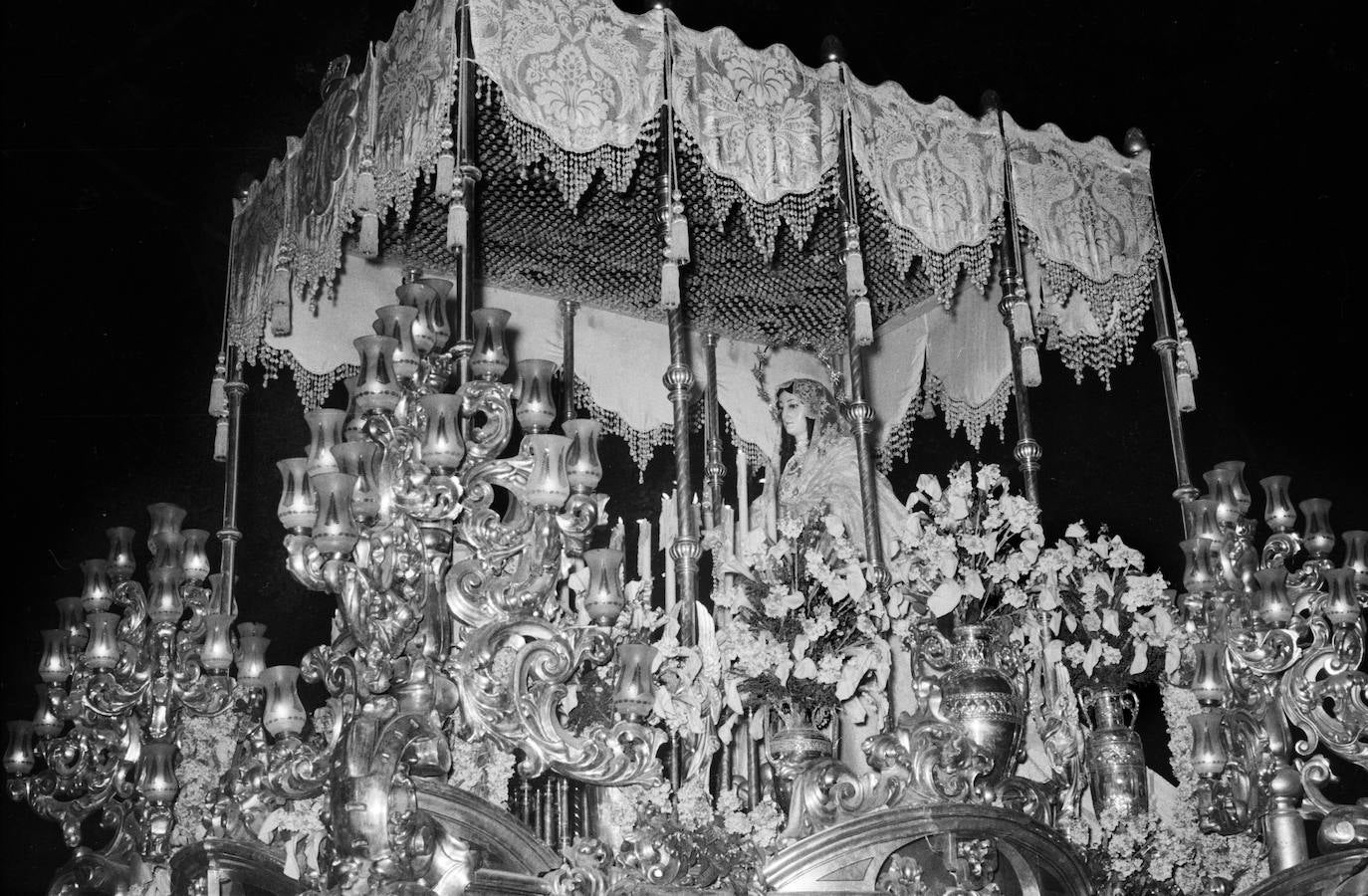 El antiguo trono de la Virgen del Rocío, de Adrián Risueño, costó 150.000 pesetas. En su ejecución, trabajaron Andrés Cabello Requena, en las labores de talla, y Luis Ramos Rosas, en los quehaceres pictóricos. El conjunto presentaba unos airosos arbotantes con tulipas.