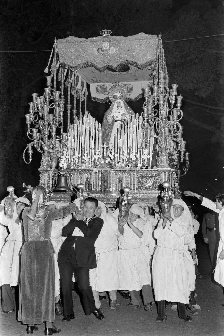 La Cofradía de la Sentencia encargó en 1965 el actual trono de la Virgen del Rosario a los talleres sevillanos de Orfebrería Villarreal, diseñado por el malagueño Juan Casielles. En la imagen se observa cómo todavía se procesionaban los misterios pintados por Revello de Toro, aunque, en esa ocasión, como decoración del interior de las bambalinas del palio.