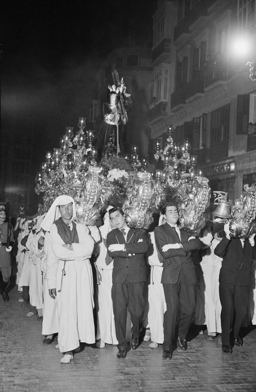 Al año 1960 se corresponde esta fotografía en la que Jesús El Rico es portado por hombres de trono ataviados con túnicas y por otros vestidos de chaqueta. Llaman poderosamente la atención las enormes cabezas de madera dorada que rematan los varales del trono.