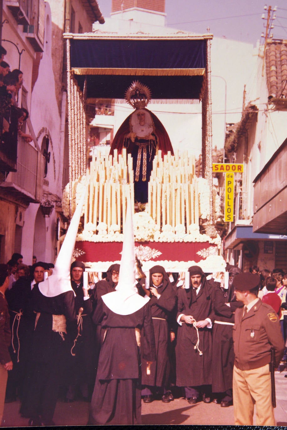 El trono de la Virgen de las Angustias discurre junto a la antigua capilla de la Piedad, en la desaparecida estrechez de la calle Cruz del Molinillo. Es el Viernes Santo 9 de abril de 1982 y la procesión se dirige por vez primera al recorrido oficial tras haber ingresado u mes antes en la Agrupación de Cofradías de Semana Santa.