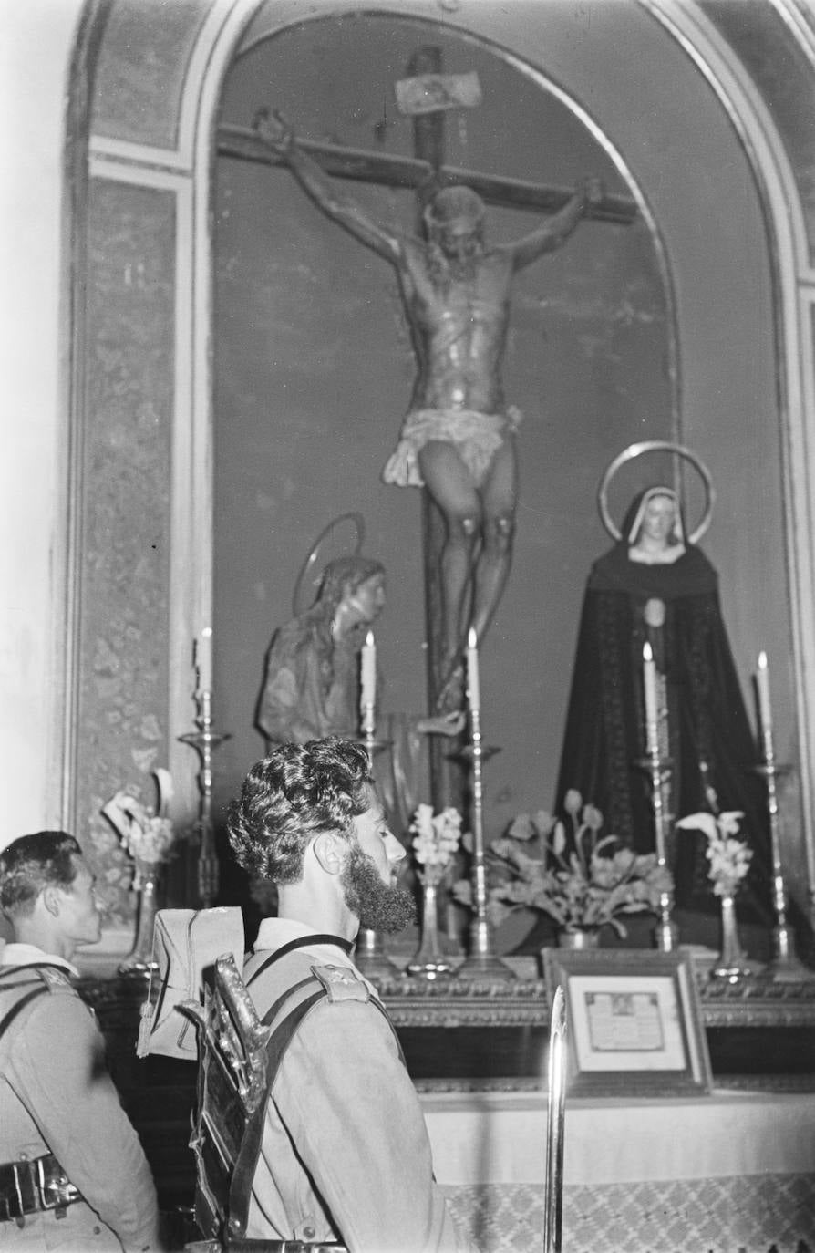 Acto con caballeros legionarios en la capilla de Santo Domingo. Las imágenes titulares están dispuestas en la embocadura de lo que hoy es el camarín en el que se encuentran habitualmente, que entonces todavía no había sido restaurado. Las paredes del recinto no han sido recubiertas aún con mármol negro, color del que viste al completo la Virgen de la Soledad, salvo la tela que enmarca su rostro.