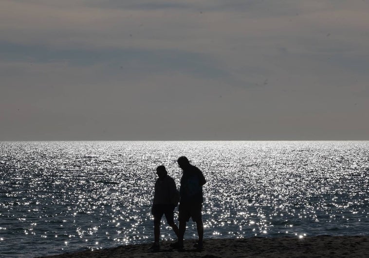 Dos personas pasean por la playa de Guadalmar con ropa de verano.