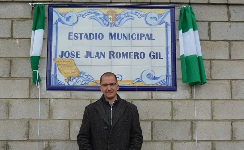 José Juan Romero posa delante de la placa donde se señala que pone nombre al campo de fútbol de Gerena, su localidad de procedencia.