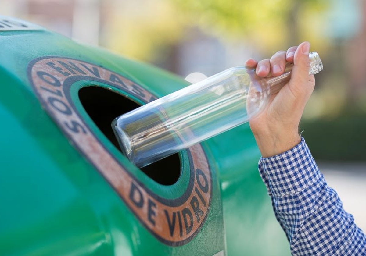 Un ciudadano deposita una botella de vidrio en el contenedor verde.