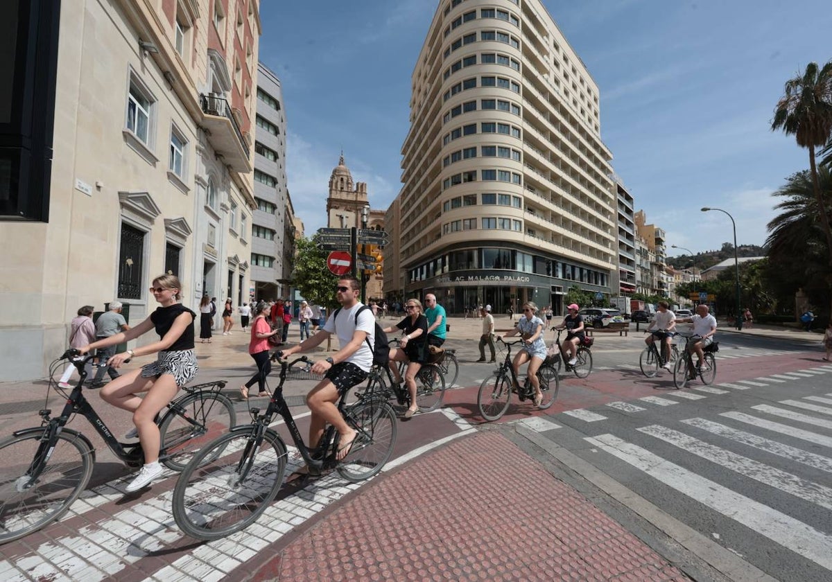 Turistas, frente al AC Málaga Palacio, recorren la ciudad en bicicleta.