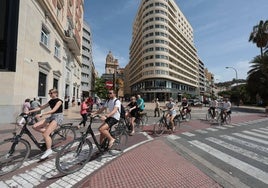 Turistas, frente al AC Málaga Palacio, recorren la ciudad en bicicleta.