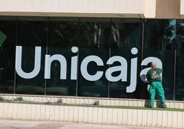 Un trabajador limpia las cristaleras de la sede de Unicaja tras haberse colocado el nuevo logo.