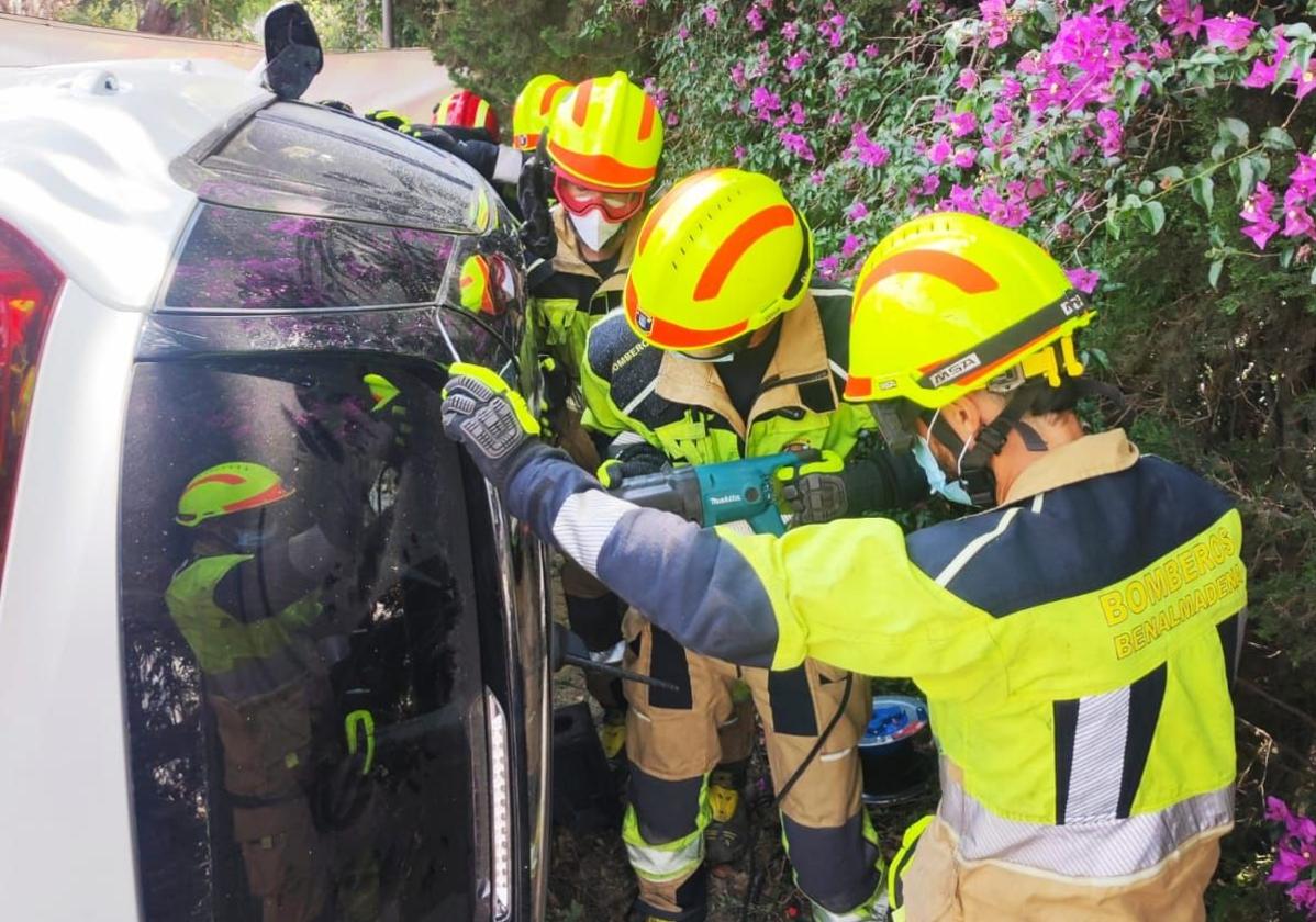 Bomberos en el lugar del siniestro, con el coche volcado.