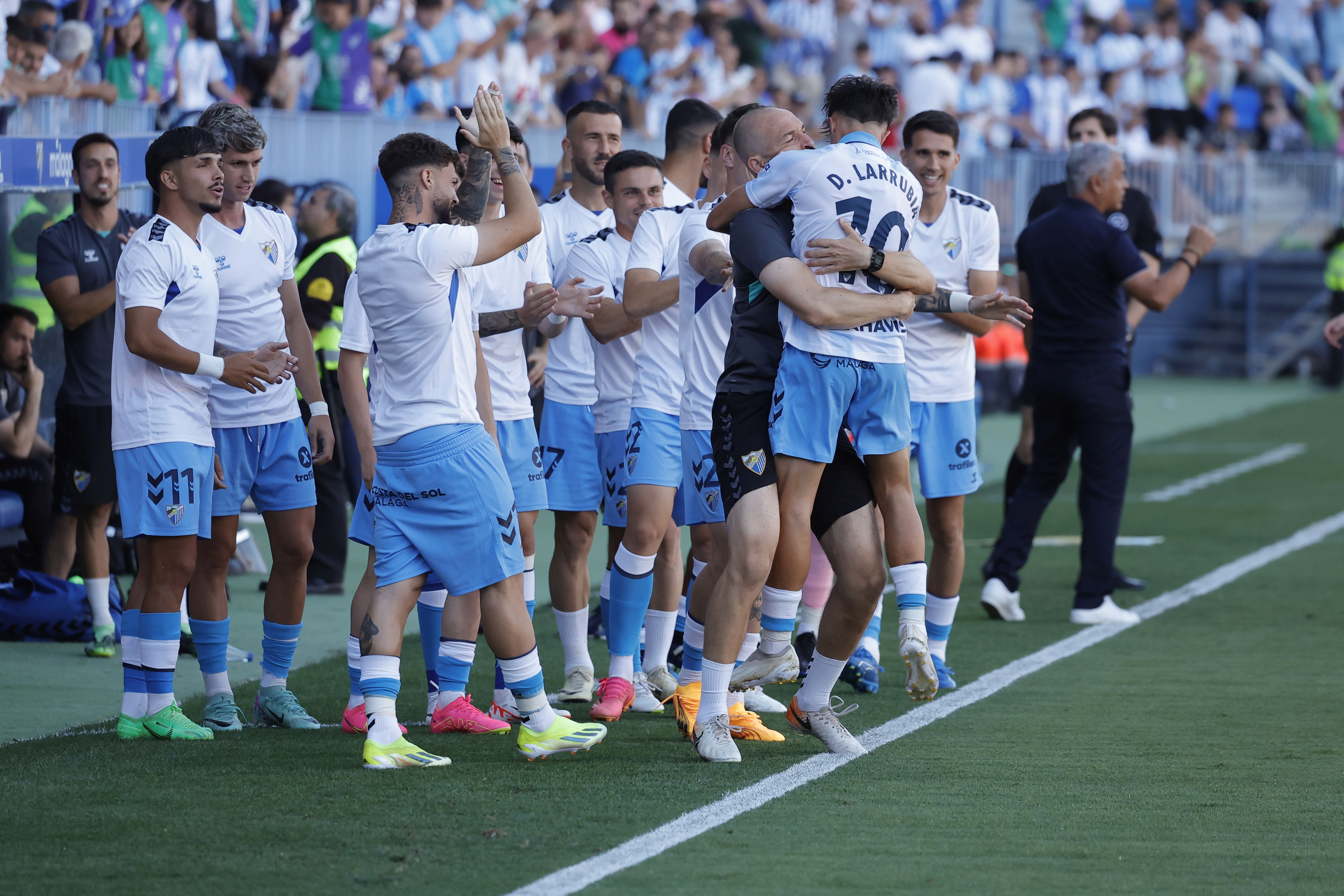 El preparador físico del Málaga, Julio Rodríguez, abraza a Larrubia tras su gol.