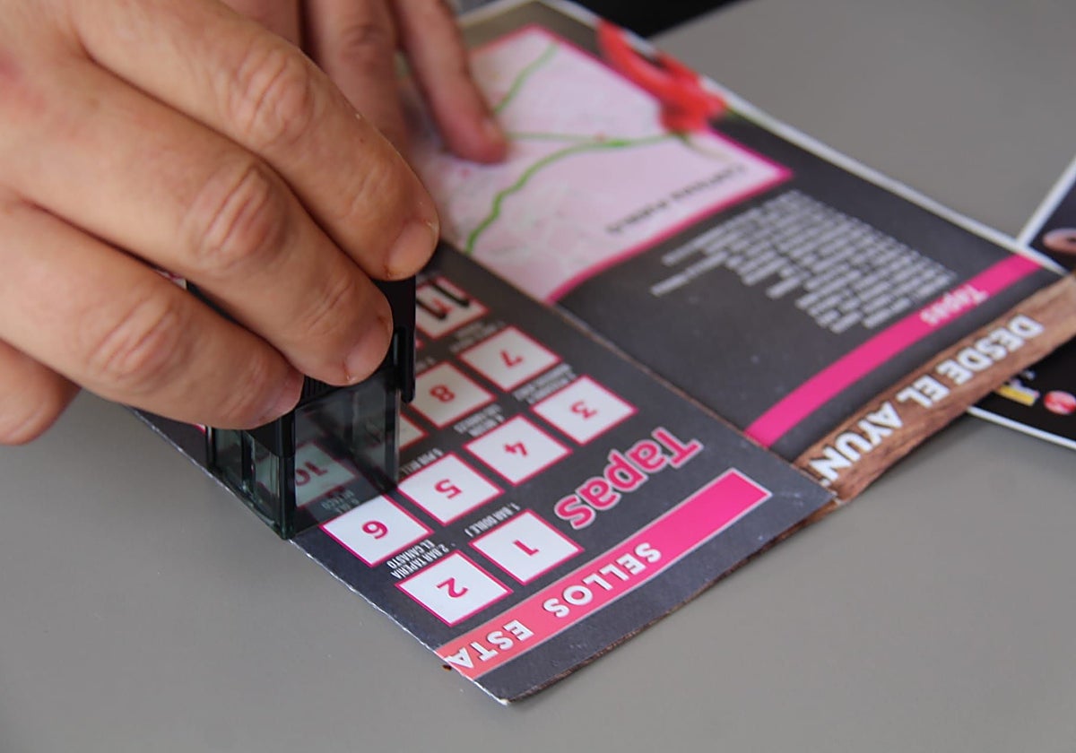 Una persona utilizando el pasaporte de sellos para votar las tapas de Cártama.