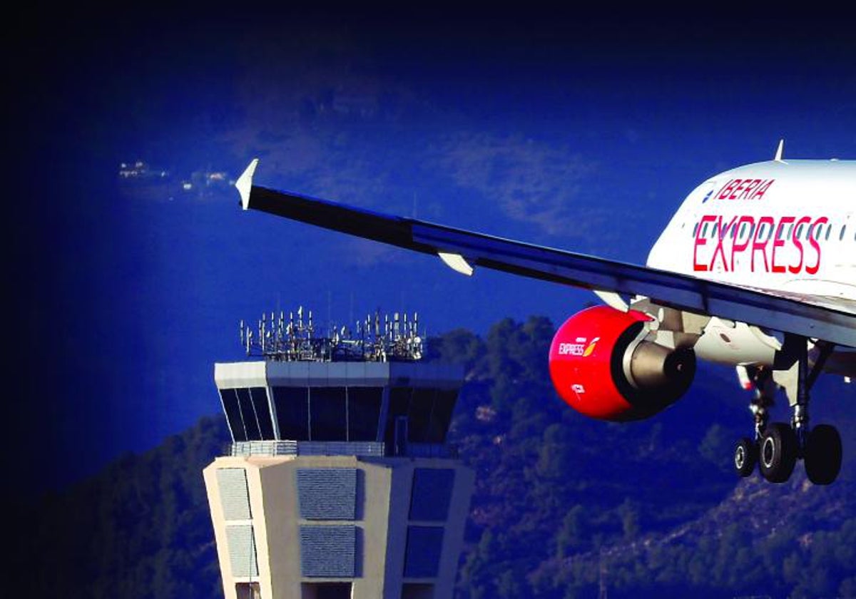 Un avión pasa por delante de la torre de control del aeropuerto de Málaga.