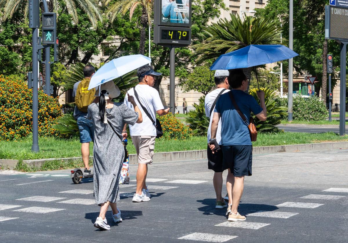 Imágenes de personas al lado de un termómetro en las calles de la capital hispalense a 47 grados de temperatura