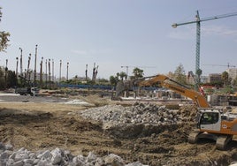 Maquinaria pesada en el solar que ocupaba el Hotel Los Álamos, junto a escombros y con las obras del nuevo complejo residencial al fondo.