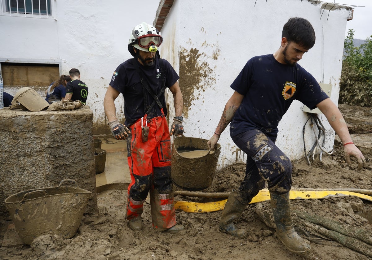 Un bombero y un voluntario de Protección Civil sacan un barreño lleno de barro.