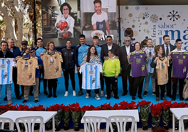 Jugadores del Málaga y directivos de la entidad posan con los ganadores del sorteo de camisetas del conjunto blanquiazul.