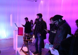 Visitantes de la exposición observan las obras mientras reproducen la narración de la Inteligencia Artificial.