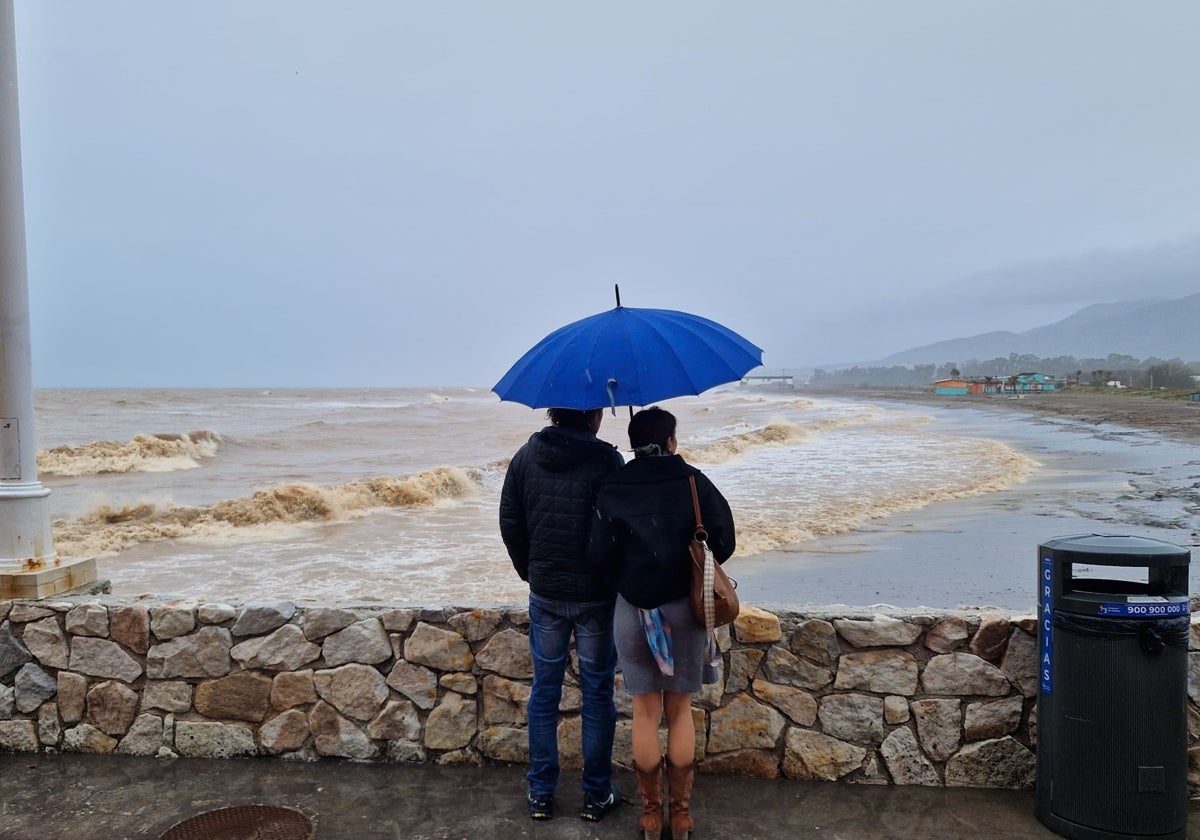 Dos personas observan el color marrón del agua del mar en Guadalmar.