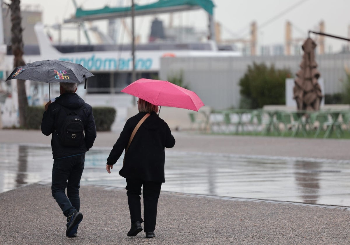 Dos turistas caminan por el Muelle Uno de Málaga bajo la lluvia.