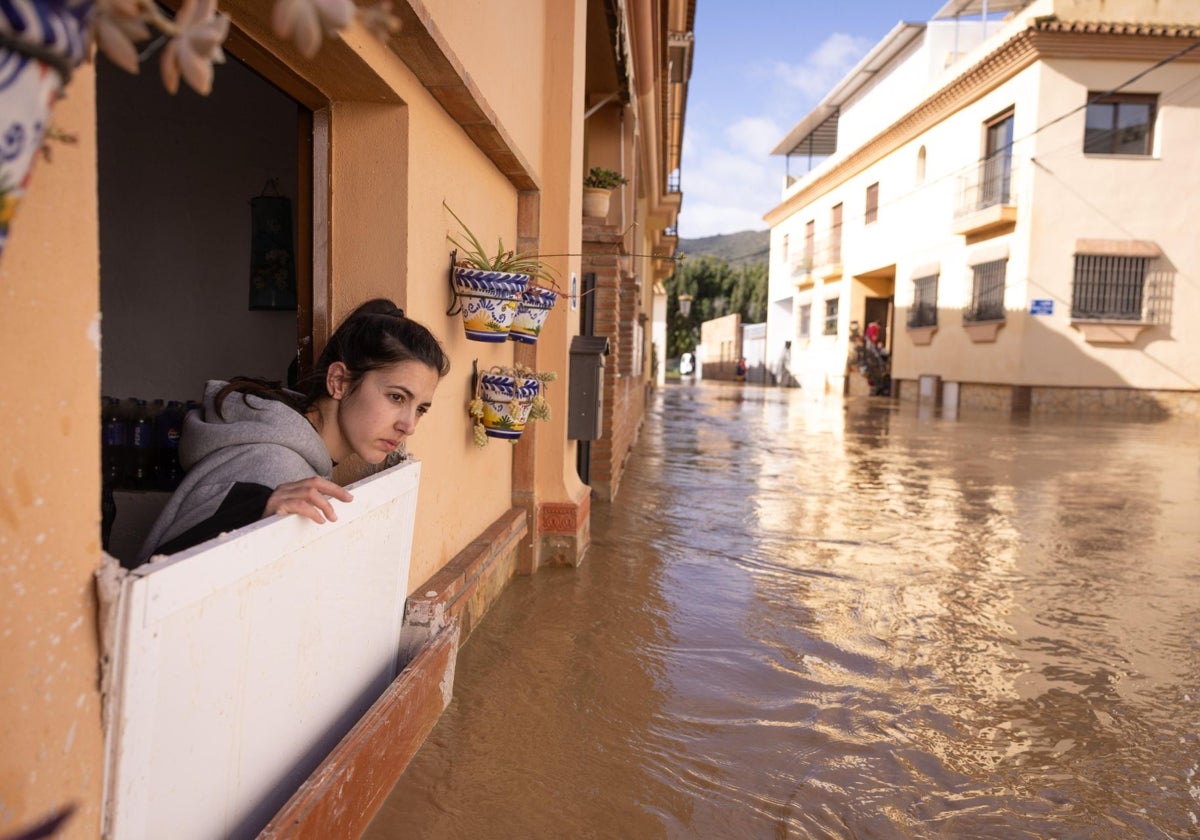 Una vecina se asoma desde su casa a la calle inundada en la barriada Doña Ana de Cártama.