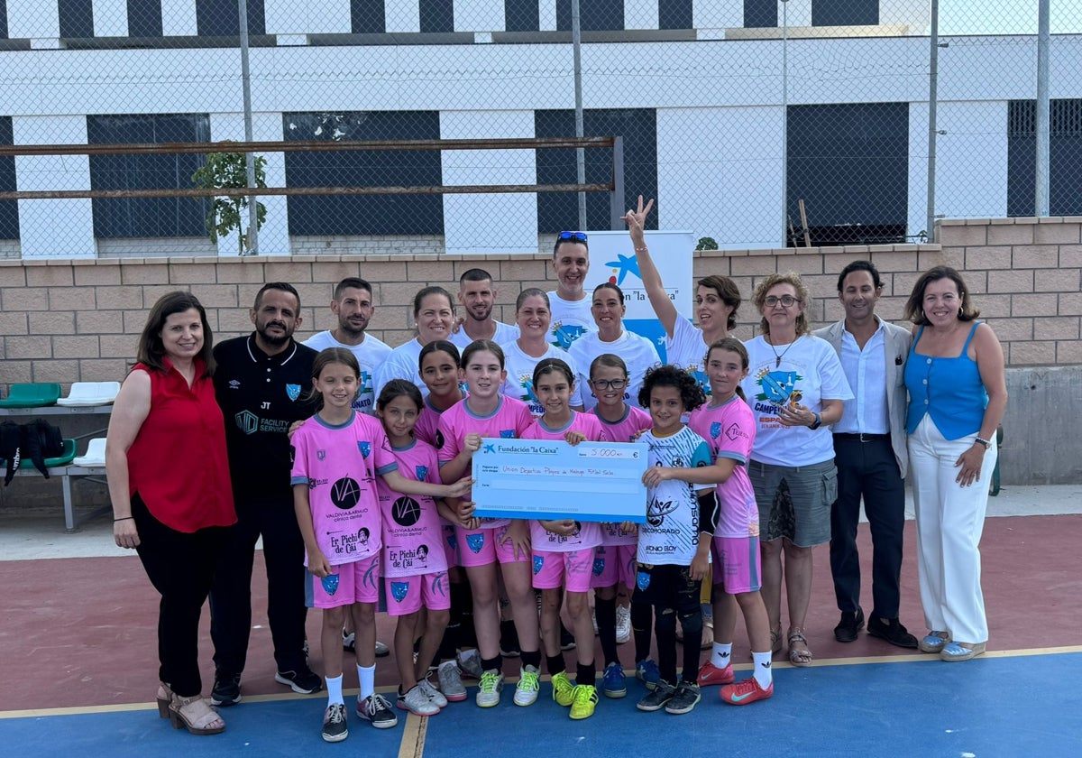 Las jugadoras del benjamín femenino del Playas de Málaga, junto con algunas madres, entrenadores y Luis Felipe Siles (segundo desde la derecha de la imagen, el Director de Área de Caixabank) sostienen el cheque entregado por la entidad para que acudan al Campeonato de España.