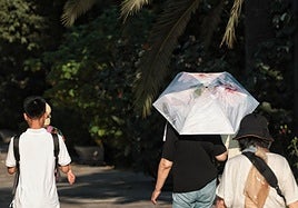 Un turista pasea bajo una sombrilla para protegerse del sol en el Parque de Málaga.