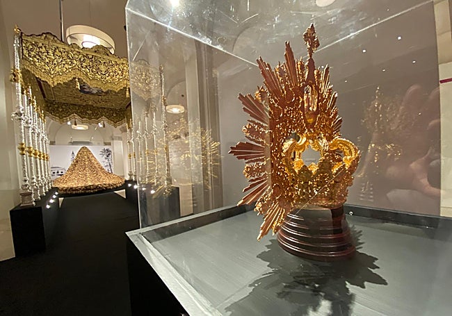 La corona, en primer término, y al fondo, el palio y manto procesional de la Virgen de la Trinidad.
